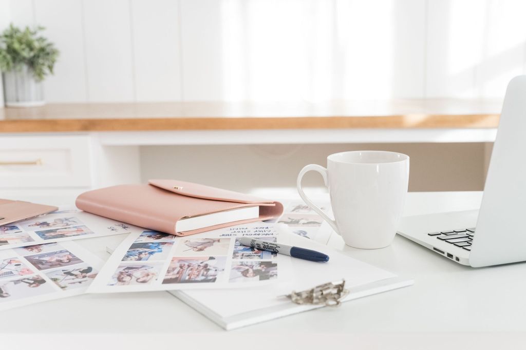 Papers, a journal, laptop and coffee mug on a desk.
